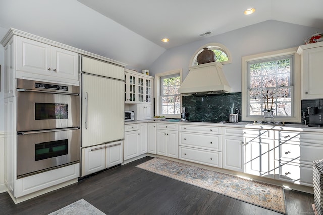 kitchen featuring double oven, white cabinetry, paneled refrigerator, and lofted ceiling