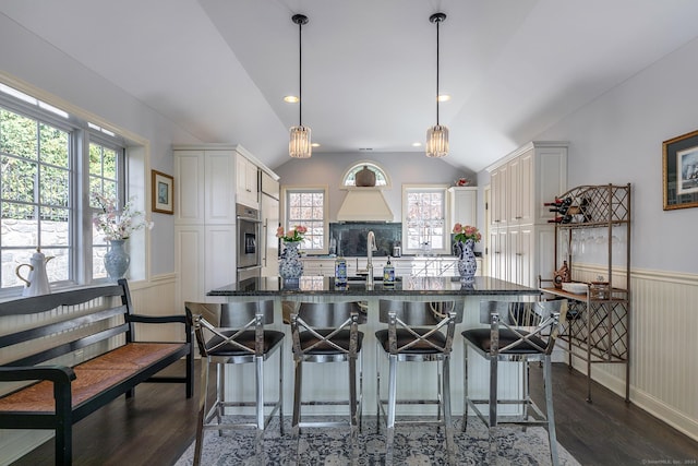 kitchen featuring lofted ceiling, oven, decorative light fixtures, a kitchen bar, and white cabinetry