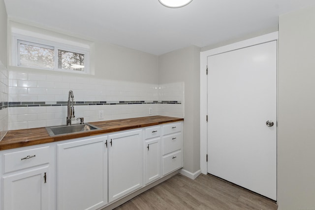 kitchen featuring wooden counters, light wood-style flooring, a sink, white cabinetry, and backsplash