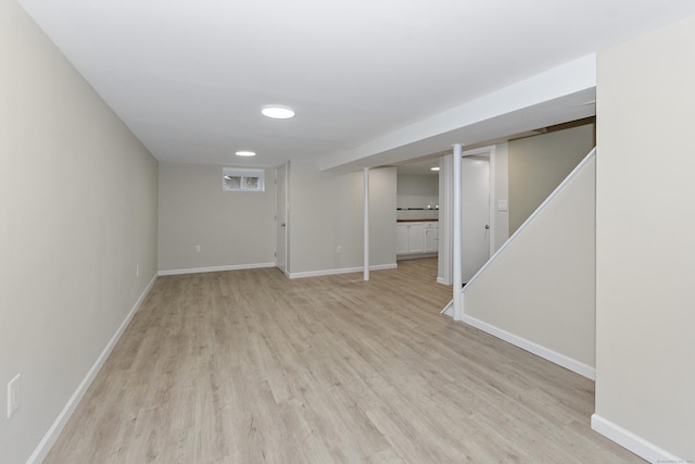 finished basement with stairway, light wood-style flooring, and baseboards