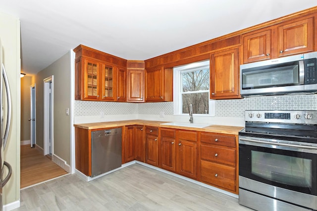 kitchen with appliances with stainless steel finishes, backsplash, light hardwood / wood-style floors, and sink