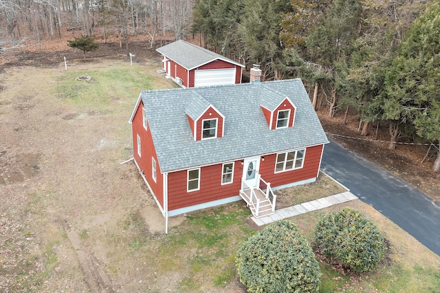 view of front of home with a shingled roof, a detached garage, a front yard, a chimney, and an outdoor structure