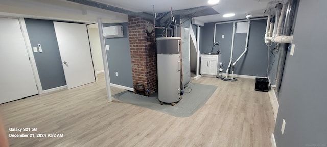 finished below grade area with an AC wall unit, a sink, light wood-style floors, baseboards, and hybrid water heater