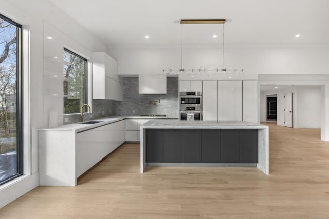 kitchen featuring backsplash, hanging light fixtures, a kitchen island, white cabinets, and sink