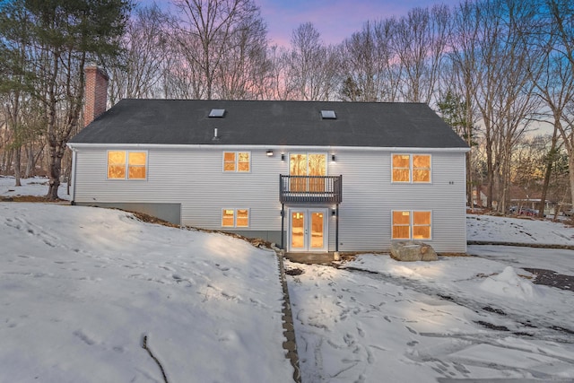 snow covered back of property with a balcony, a garage, a chimney, and french doors