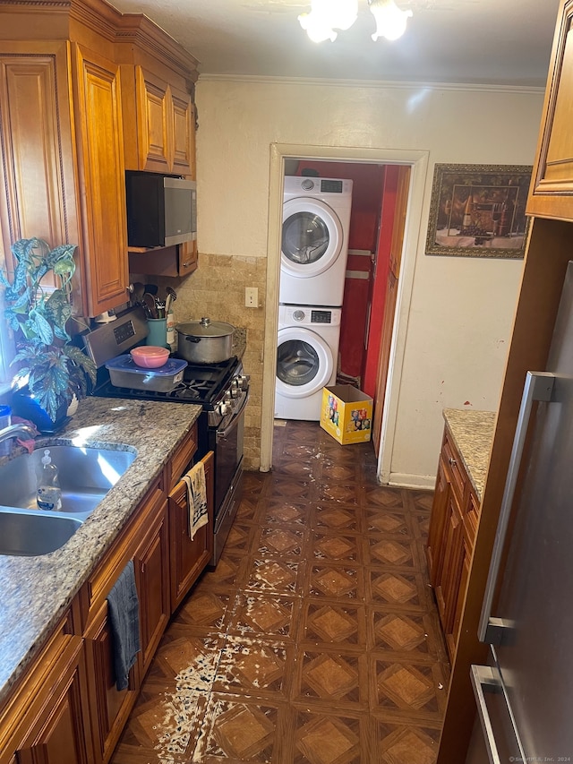 kitchen with light stone countertops, sink, stacked washer / dryer, and stainless steel appliances