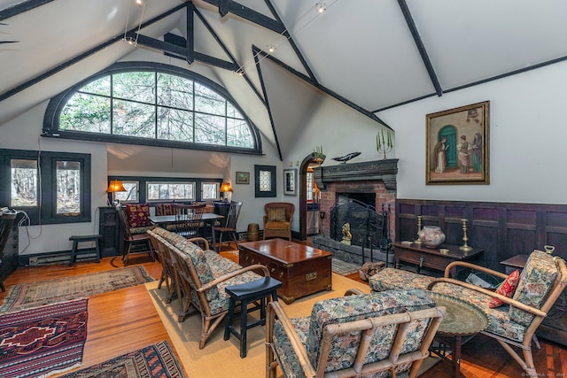 living room with high vaulted ceiling, beamed ceiling, hardwood / wood-style flooring, and a brick fireplace