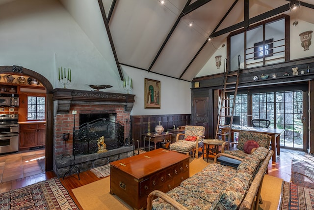 living room featuring high vaulted ceiling, wood-type flooring, a healthy amount of sunlight, and a brick fireplace