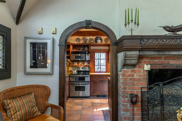 bar with stainless steel appliances, light tile patterned floors, backsplash, a fireplace, and vaulted ceiling with beams