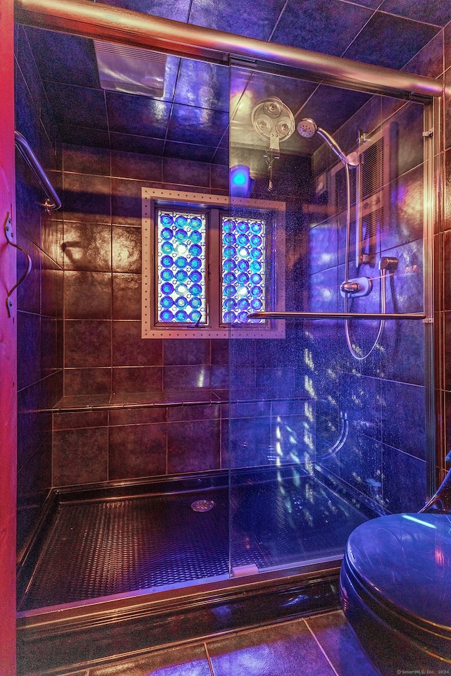 bathroom featuring toilet, tile patterned flooring, and a tile shower