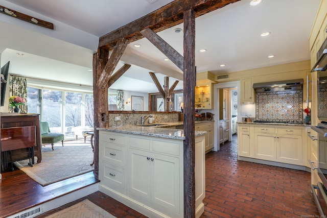 kitchen featuring light stone countertops, sink, tasteful backsplash, range hood, and black stovetop