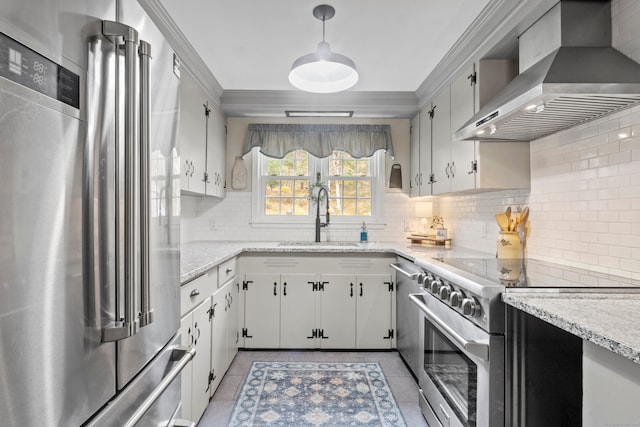 kitchen featuring stainless steel appliances, white cabinetry, sink, wall chimney exhaust hood, and hanging light fixtures