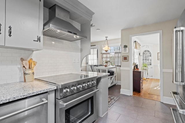 kitchen featuring appliances with stainless steel finishes, wall chimney exhaust hood, decorative light fixtures, light wood-type flooring, and decorative backsplash