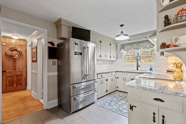 kitchen featuring high end refrigerator, white cabinetry, light stone counters, backsplash, and pendant lighting