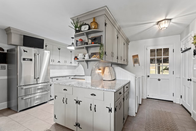 kitchen with light stone counters, light tile patterned floors, high quality fridge, and backsplash