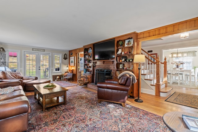 living room with hardwood / wood-style flooring, ornamental molding, a fireplace, a chandelier, and french doors