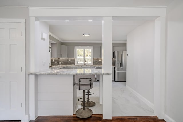 kitchen with sink, a kitchen breakfast bar, backsplash, stainless steel fridge, and gray cabinets