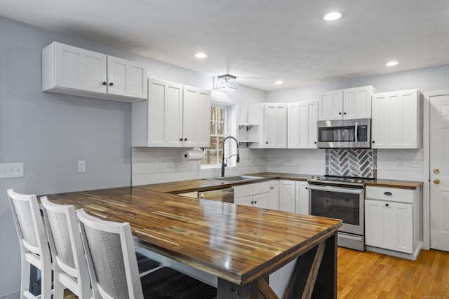 kitchen with butcher block countertops, white cabinetry, and stainless steel appliances