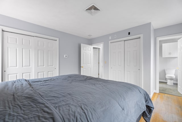 bedroom featuring two closets, light hardwood / wood-style floors, and ensuite bathroom