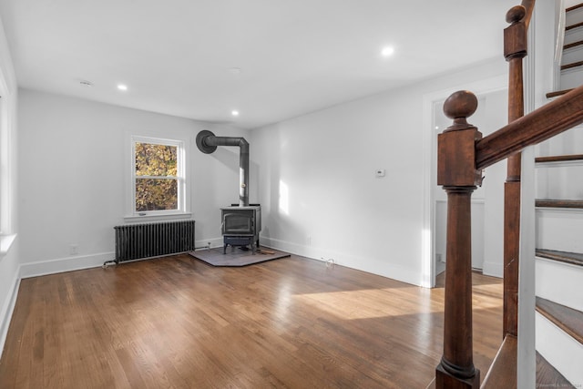 unfurnished living room with radiator heating unit, a wood stove, and wood-type flooring