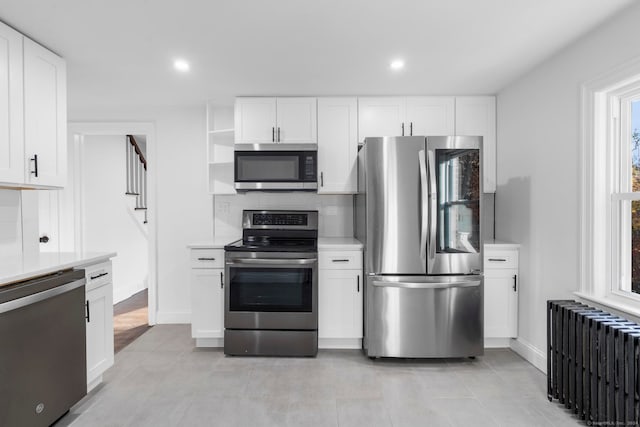 kitchen with stainless steel appliances, white cabinets, and radiator heating unit