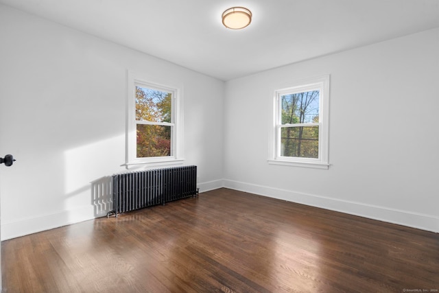 empty room featuring radiator, a healthy amount of sunlight, and dark hardwood / wood-style floors