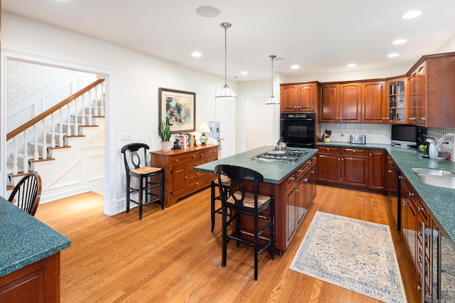 kitchen with stainless steel gas cooktop, a center island, light hardwood / wood-style floors, black oven, and a breakfast bar area