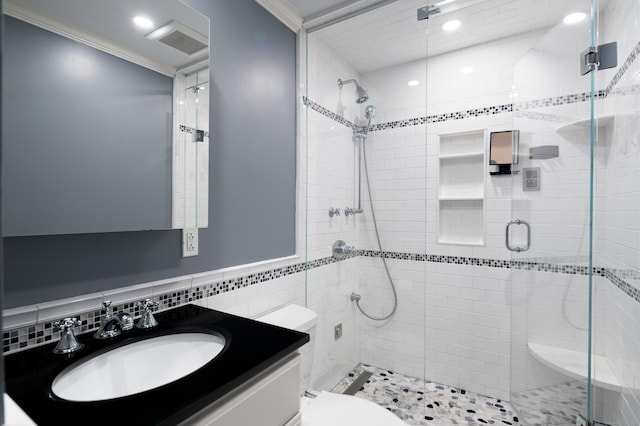 bathroom featuring vanity, a shower with door, toilet, ornamental molding, and tile walls