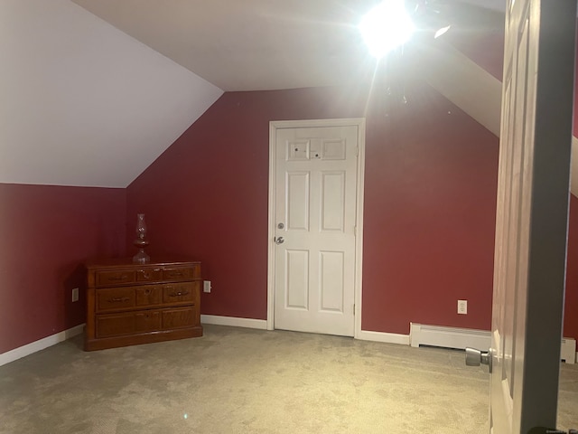 additional living space with a baseboard heating unit, light colored carpet, and vaulted ceiling