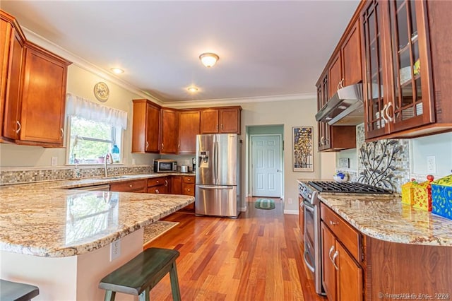 kitchen featuring sink, a breakfast bar area, stainless steel appliances, light hardwood / wood-style flooring, and ventilation hood