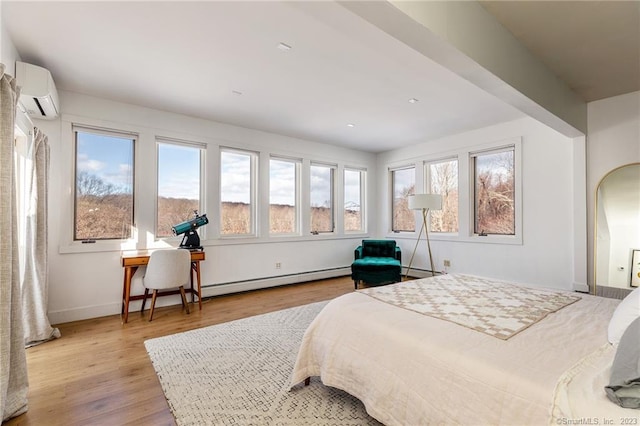 bedroom featuring baseboard heating, a wall unit AC, and light wood-type flooring