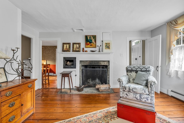 living room with a fireplace, hardwood / wood-style flooring, visible vents, and a baseboard heating unit
