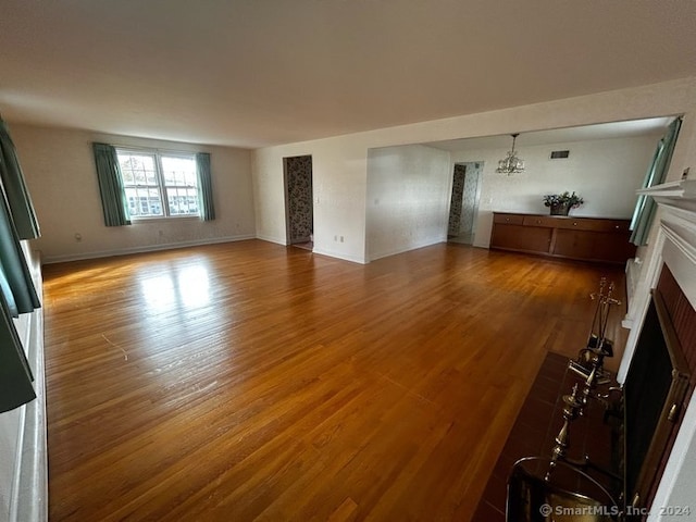 unfurnished living room featuring hardwood / wood-style floors, a chandelier, and a brick fireplace