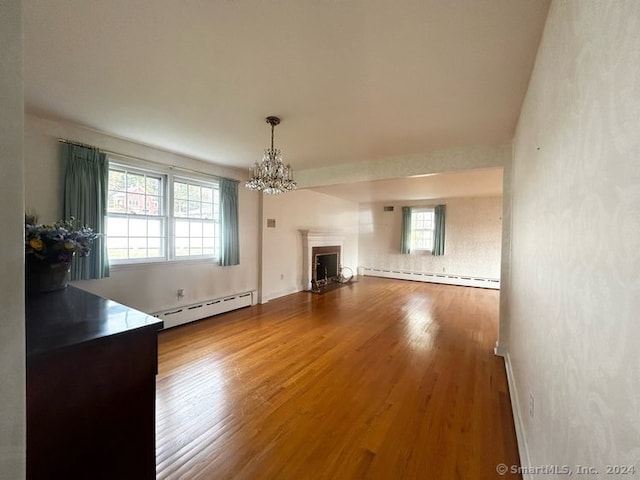 unfurnished living room with baseboard heating, a wealth of natural light, and hardwood / wood-style flooring