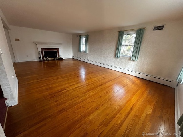 unfurnished living room featuring a fireplace, wood-type flooring, and a baseboard heating unit