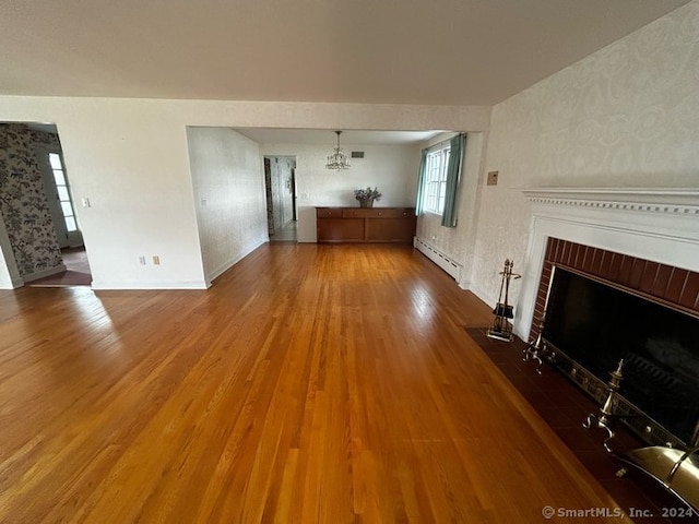 unfurnished living room featuring wood-type flooring, an inviting chandelier, a brick fireplace, and a baseboard heating unit