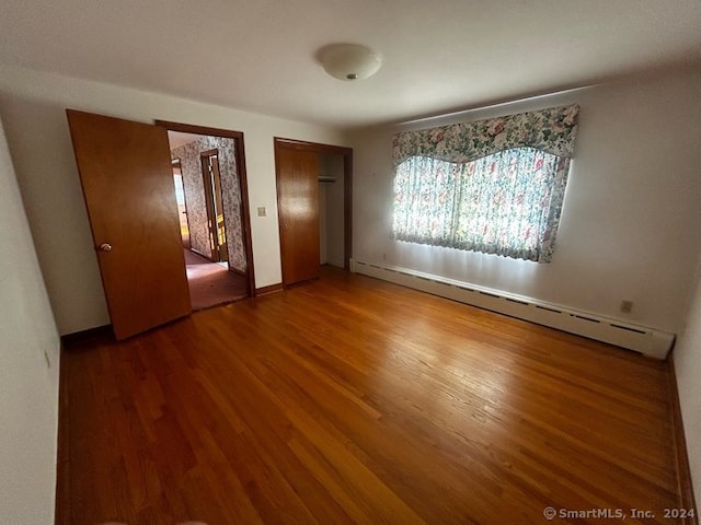 unfurnished bedroom featuring a baseboard heating unit and hardwood / wood-style flooring