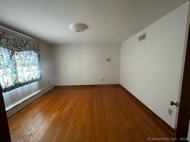 empty room with hardwood / wood-style floors and a baseboard radiator