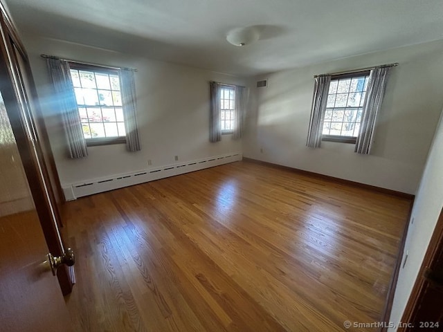 spare room featuring wood-type flooring, a baseboard radiator, and a wealth of natural light