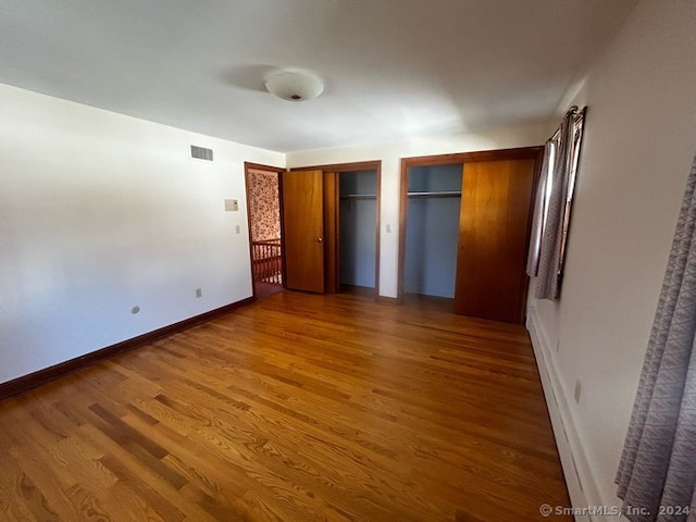 unfurnished bedroom featuring multiple closets and hardwood / wood-style floors