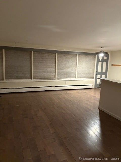 empty room with dark wood-type flooring and a baseboard heating unit