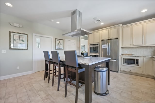 kitchen featuring stainless steel appliances, light stone counters, island range hood, a center island, and cream cabinetry