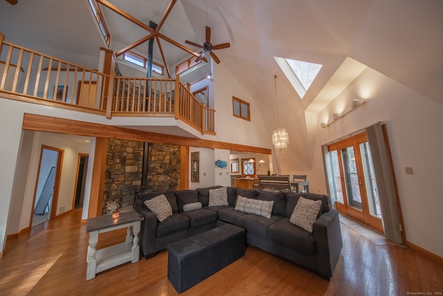 living room with ceiling fan with notable chandelier, a skylight, high vaulted ceiling, hardwood / wood-style floors, and a wood stove