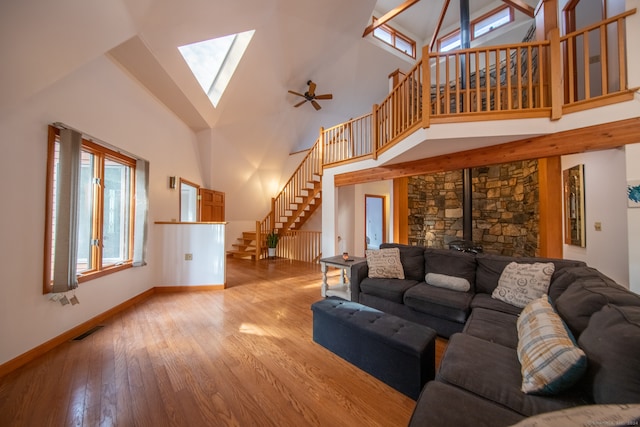 living room with ceiling fan, a wood stove, high vaulted ceiling, and light hardwood / wood-style flooring