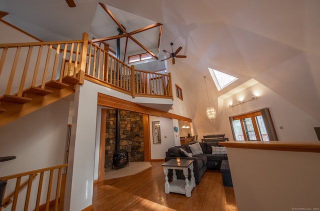 living room featuring wood-type flooring, a skylight, a wood stove, and high vaulted ceiling