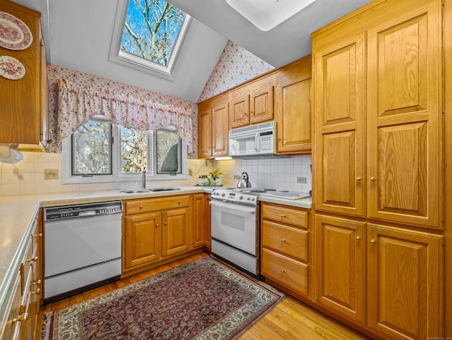 kitchen with lofted ceiling with skylight, white appliances, sink, light hardwood / wood-style flooring, and tasteful backsplash