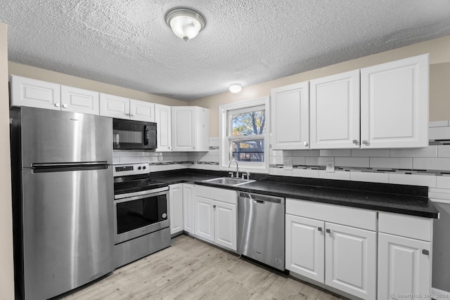 kitchen with stainless steel appliances, white cabinets, decorative backsplash, sink, and light hardwood / wood-style flooring