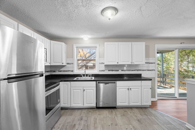 kitchen featuring stainless steel appliances, light hardwood / wood-style floors, white cabinets, decorative backsplash, and sink