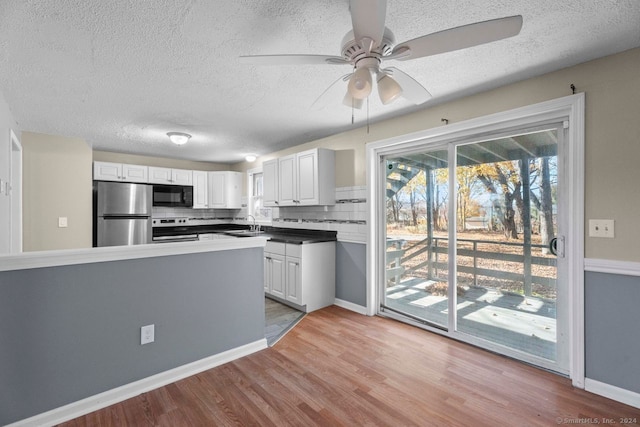 kitchen featuring light hardwood / wood-style floors, appliances with stainless steel finishes, a textured ceiling, white cabinets, and decorative backsplash