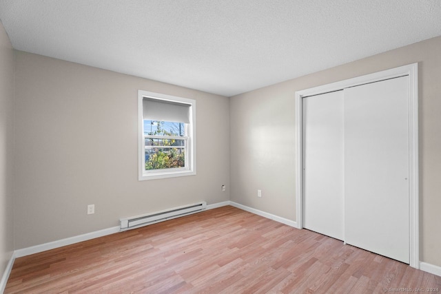 unfurnished bedroom with a closet, a textured ceiling, baseboard heating, and light hardwood / wood-style floors